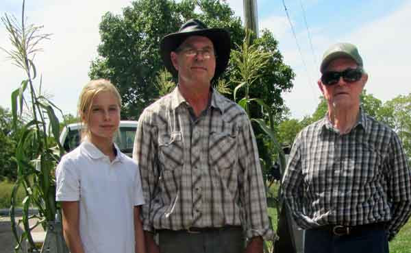 Three generations of farmers standing in front of their crop: A young girl about ten years old, a middle aged man, and a senior man.